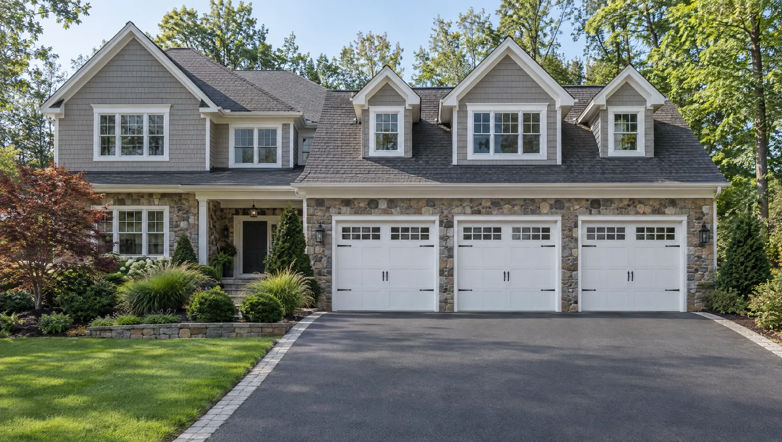 Stone and shingle home with three white carriage-style garage doors